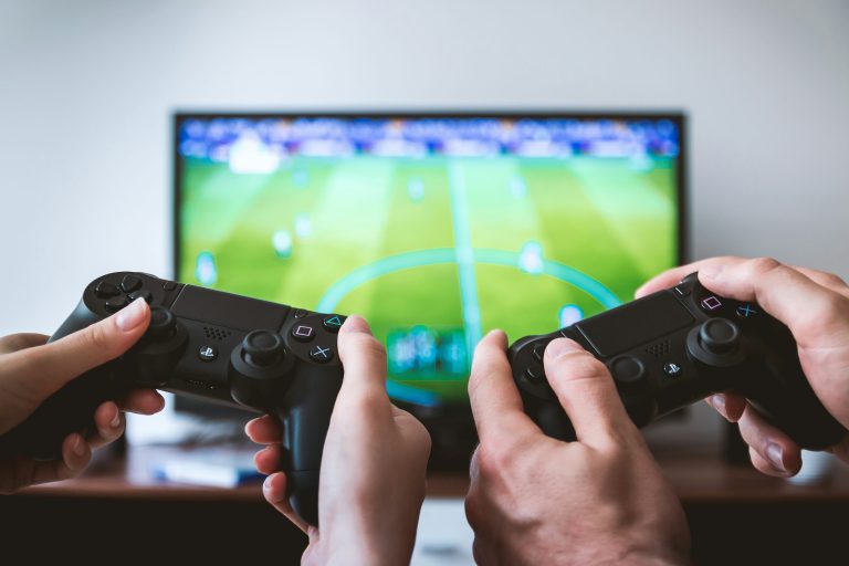 Dua orang bermain game menggunakan controller PlayStation, mencerminkan peluang mendapatkan cuan dari dunia gaming, seperti streaming, turnamen esports, dan jual beli akun game.