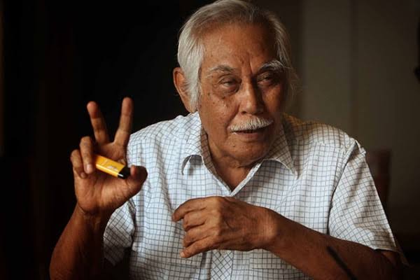 Potret Bob Sadino dengan gaya khas kemeja dan celana pendek, simbol pengusaha sukses yang sederhana dan inspiratif di Indonesia.